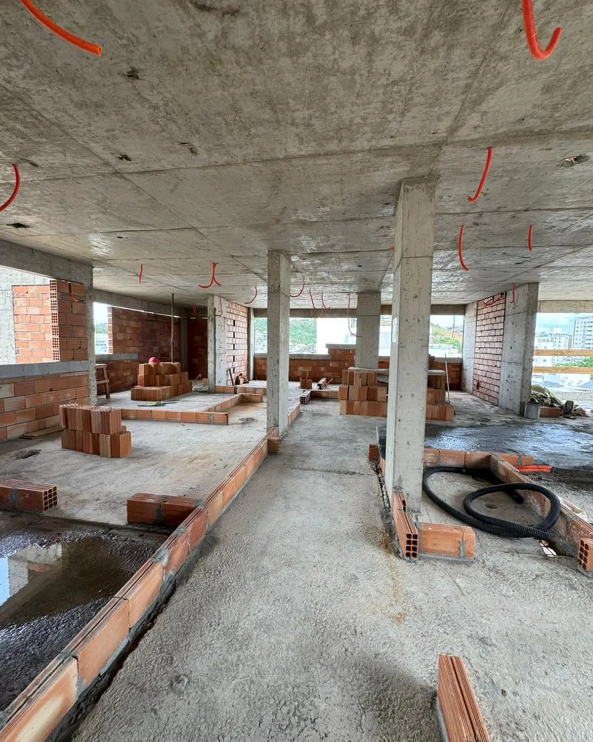 Pavimento em construção: laje e pilares de concreto aparentes, alvenaria sendo levantada e eletrodutos pendurados no teto.
